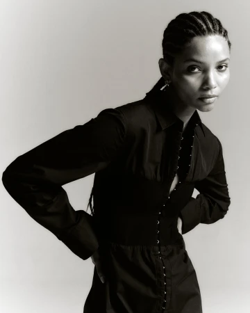 A stunning portrait of a Black woman with braided hair, wearing a stylish black shirt and corset, posing against a light background.