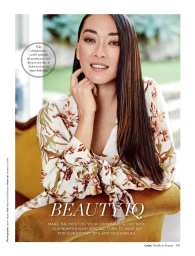 Portrait of a smiling woman with long brown hair wearing a floral top while leaning on an ochre armchair