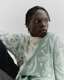Black man wearing a patterned mint green and white cardigan with braided hair against a plain background