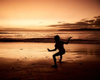Silhouette of a person dancing on a wet sandy beach during a warm sunset by Klint Collier in Sydney.