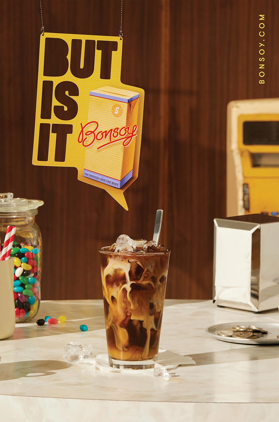 Iced latte with ice cubes next to a glass jar of jelly beans on a marble counter in front of a brown wood-paneled wall.