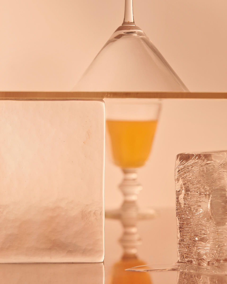 Still life of a cocktail glass, juice, ice cubes, and frosted glass, featuring a blend of textures and colors in an indoor setting.