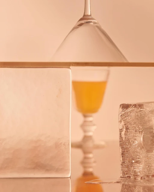 Still life of a cocktail glass, juice, ice cubes, and frosted glass, featuring a blend of textures and colors in an indoor setting.