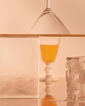 Still life of a cocktail glass, juice, ice cubes, and frosted glass, featuring a blend of textures and colors in an indoor setting.