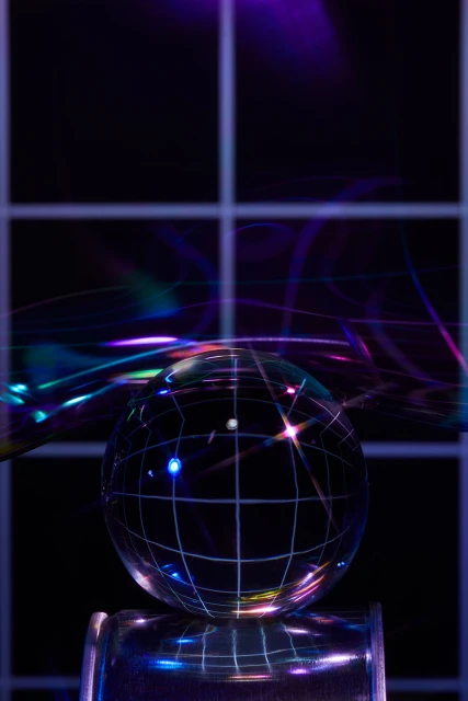 Abstract photograph of a crystal ball with a grid pattern, resting on a metallic cylinder against a dark background with neon light effects.