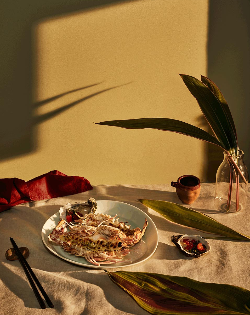 Seafood dish with grilled slipper lobster served on a white plate, complete with sauce, chopsticks, and decorative leaves.