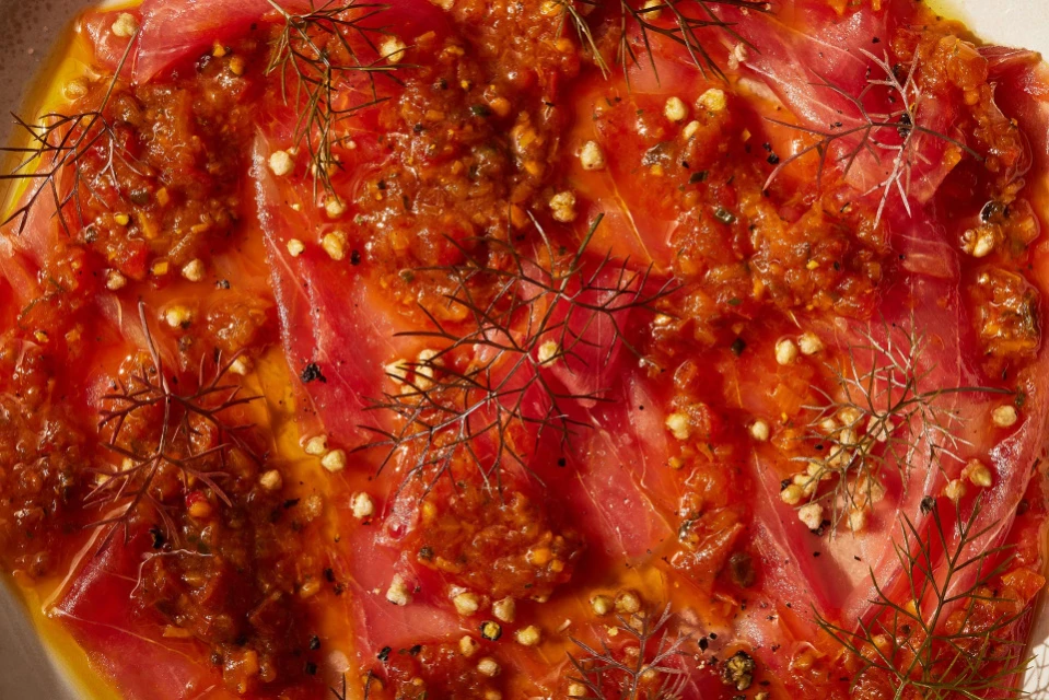 Overhead shot of a vibrant tuna carpaccio dish drizzled with oil, topped with a rich sauce, and garnished with dill sprigs.