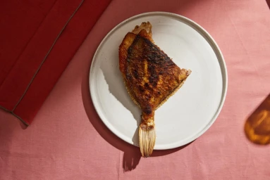 Top-down view of a crisp pan-seared fish on a white ceramic plate over a pink textured tablecloth.