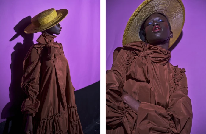 Model in brown high-collar dress and wide-brim yellow straw hat posing against purple background by Henry Lou