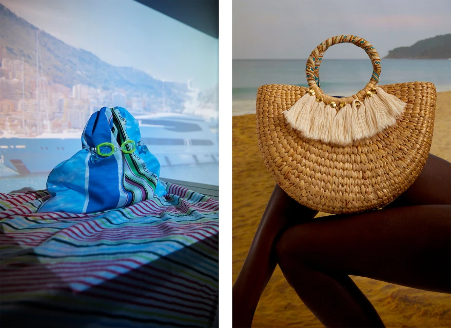 Two beach bags on striped blankets, one straw and the other blue, evoking a vacation mood with sand, ocean, and boats in the background.