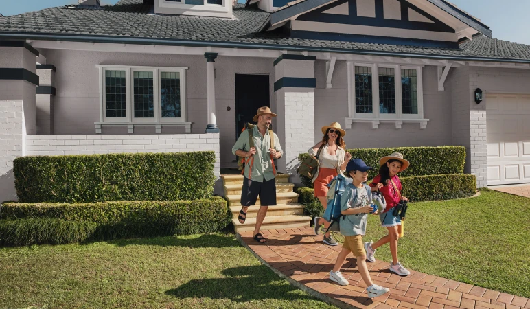 Family of four walks down the steps of their house for a day trip, wearing hats, backpacks, and carrying binoculars, outdoors on a sunny day.