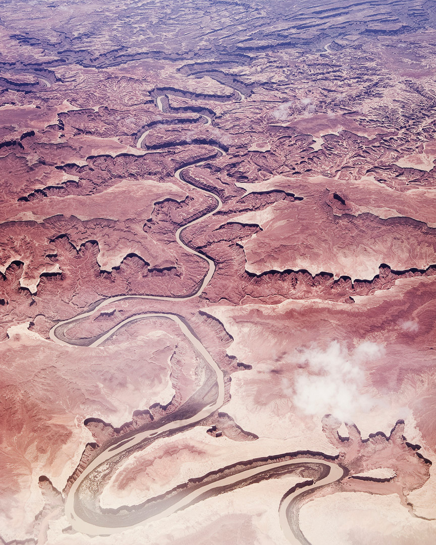 Aerial view of a winding river cutting through a vast desert landscape with reddish rock formations and sparse vegetation, creating a textured scene.
