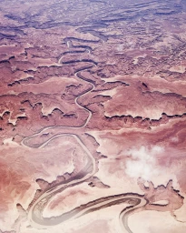 High-altitude aerial view of a winding river cutting through an expansive desert canyon landscape with rugged terrain.