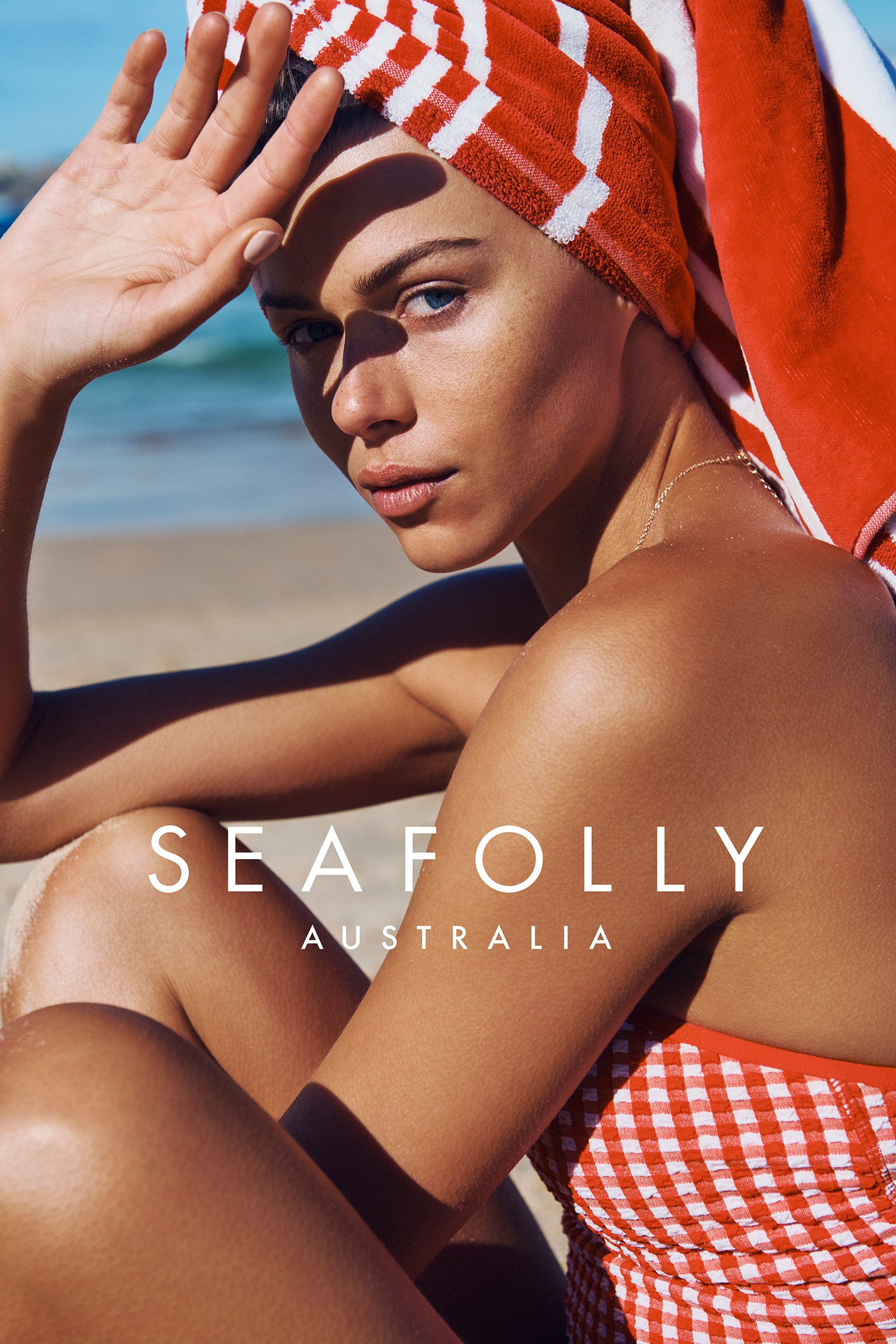 Close-up of a woman on a beach wearing a red and white towel on her head and a red and white checkered swimsuit.