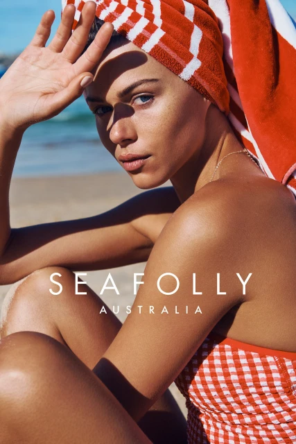 Close-up of a woman on a beach wearing a red and white towel on her head and a red and white checkered swimsuit.