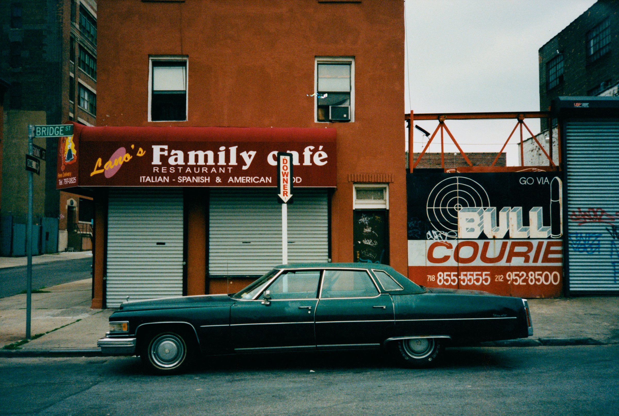 Classic dark green sedan parked outside Lano's Family Cafe restaurant. Building with Bull Courie sign in urban street scene.