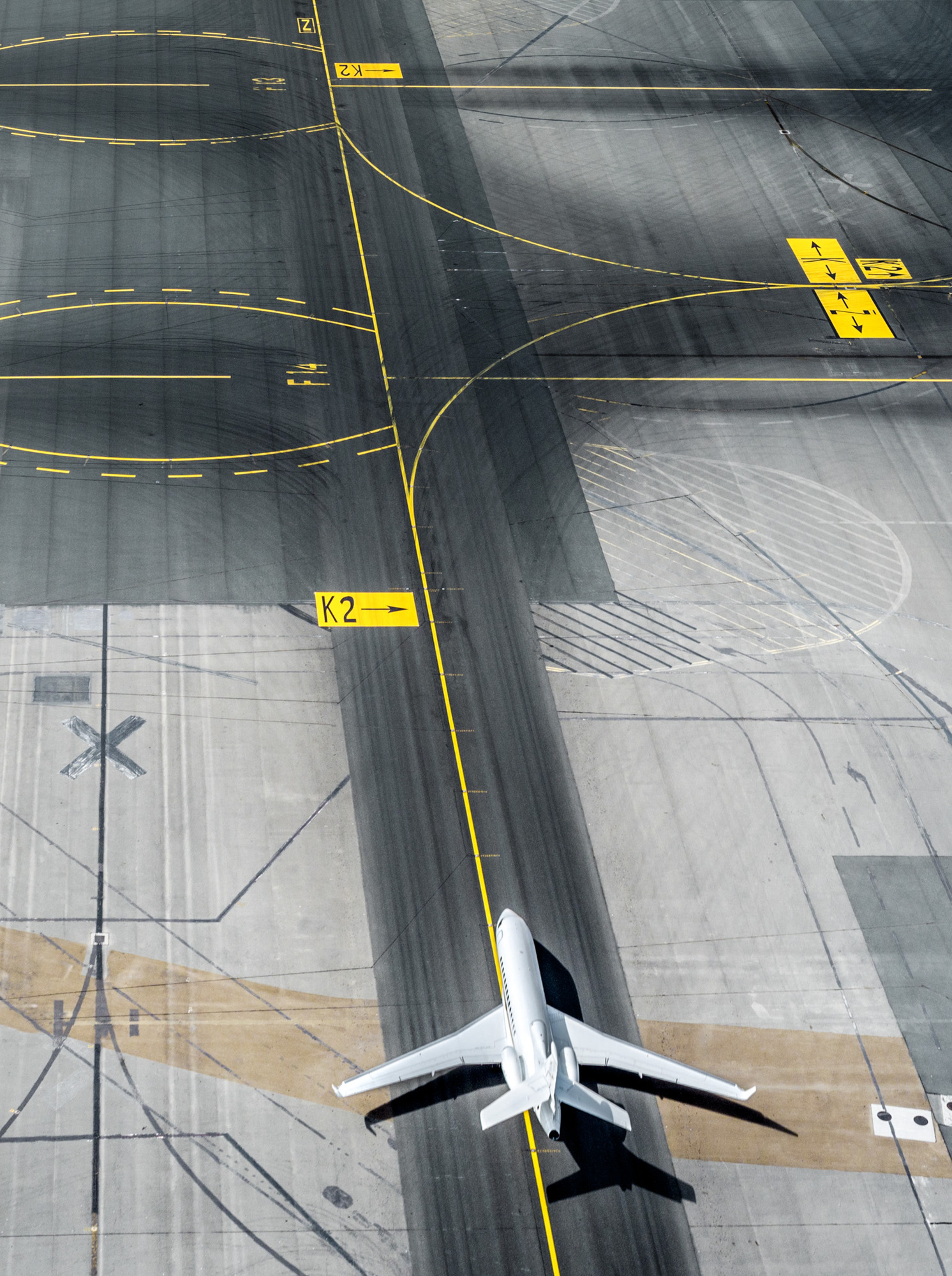 Aerial view of a white private jet on the tarmac of an airport runway with yellow markings and various directions signage.
