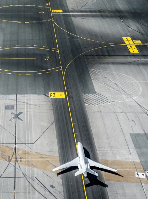 Aerial view of a white private jet on the tarmac of an airport runway with yellow markings and various directions signage.