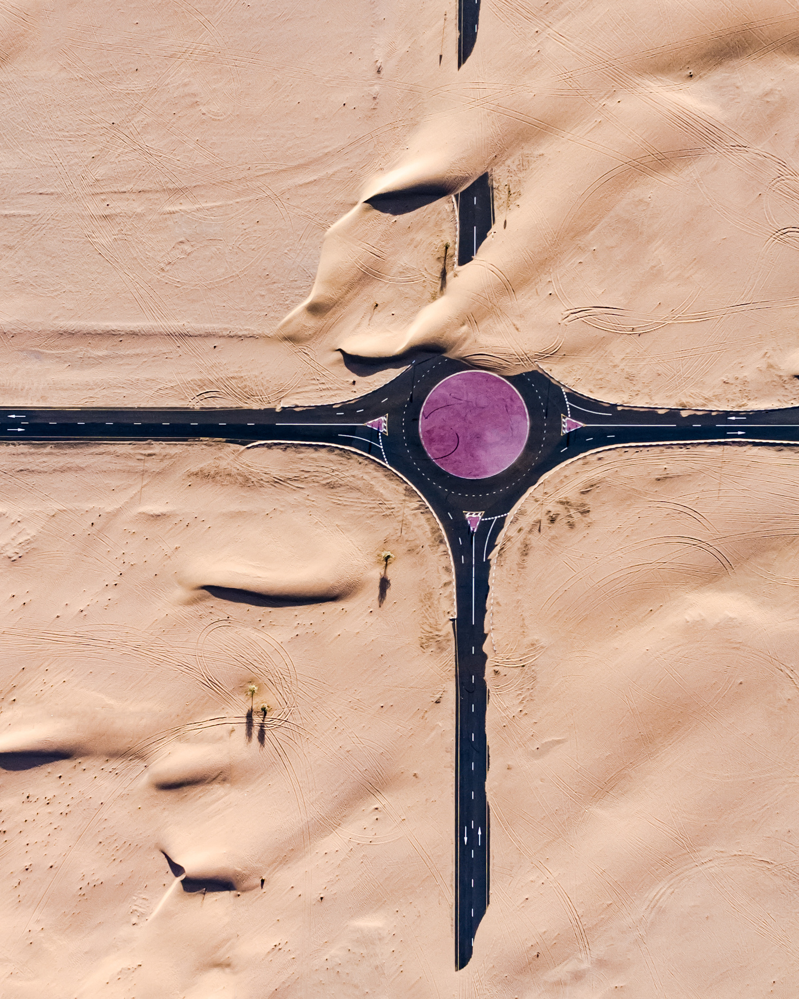 Aerial view of desert landscape with a roundabout and roads creating a cross shape, showcasing travel and architectural design.