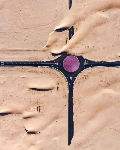 Aerial view of desert landscape with a roundabout and roads creating a cross shape, showcasing travel and architectural design.