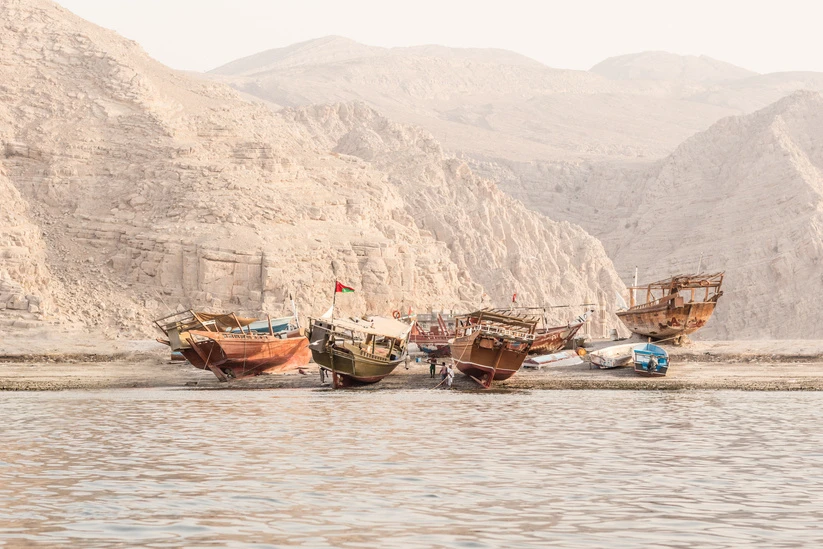 Several wooden fishing boats resting on the sand with water in the foreground and mountains in the background, creating a scenic seascape.