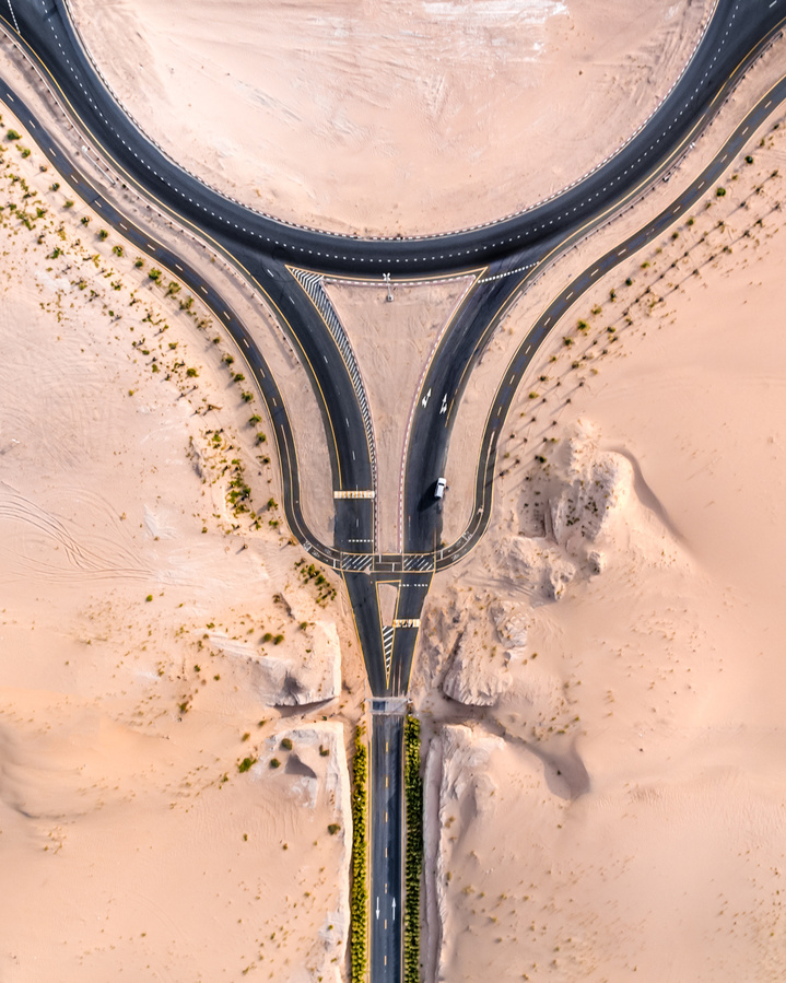Aerial view of an abstract highway interchange with desert landscape and sparse vegetation on either side, captured from above.