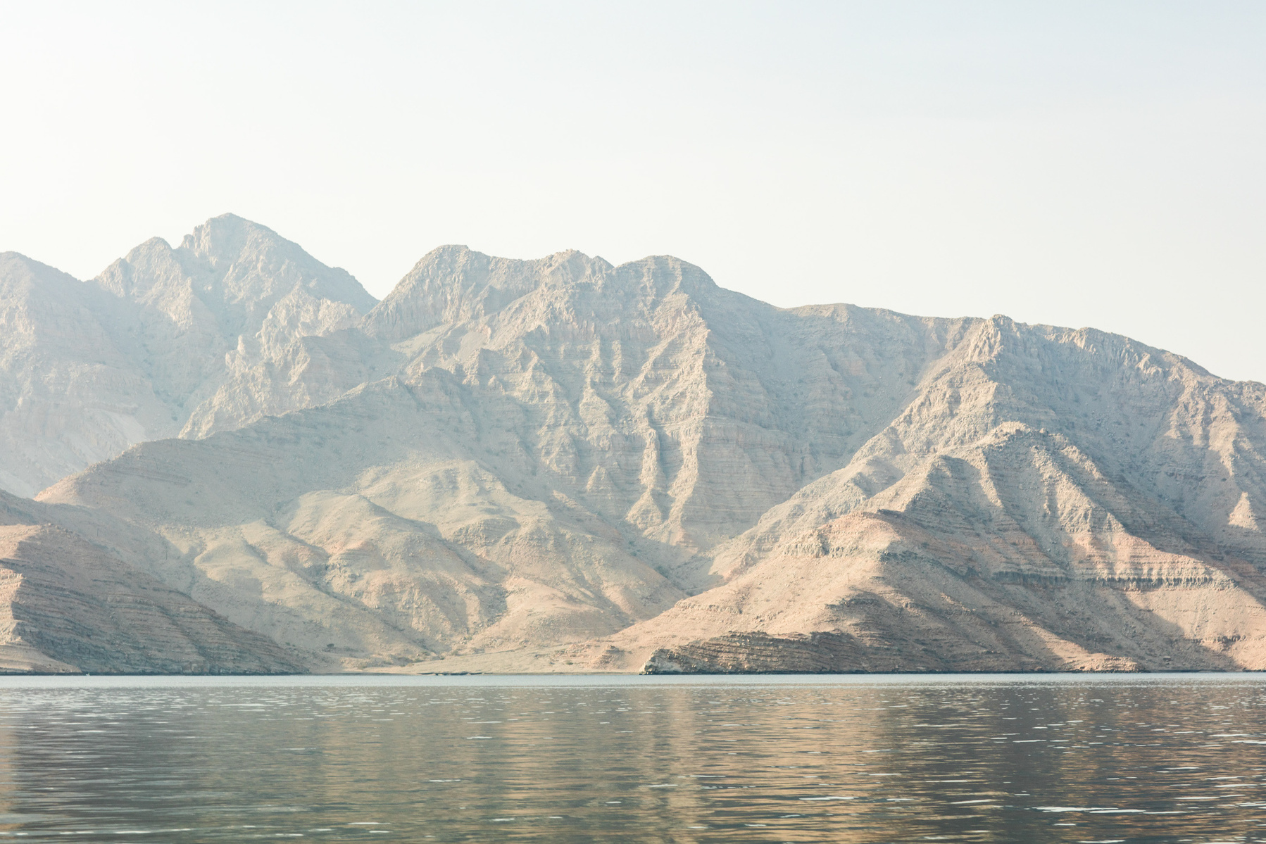 Scenic vista of rugged mountains sloping down toward still water under a clear sky, evoking a sense of natural beauty and tranquility.