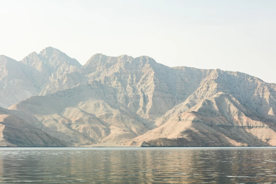 Scenic vista of rugged mountains sloping down toward still water under a clear sky, evoking a sense of natural beauty and tranquility.