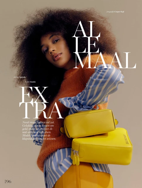 Fashion editorial image featuring a stylish woman with an afro hairstyle wearing an orange sweater and blue striped shirt, holding yellow purses.