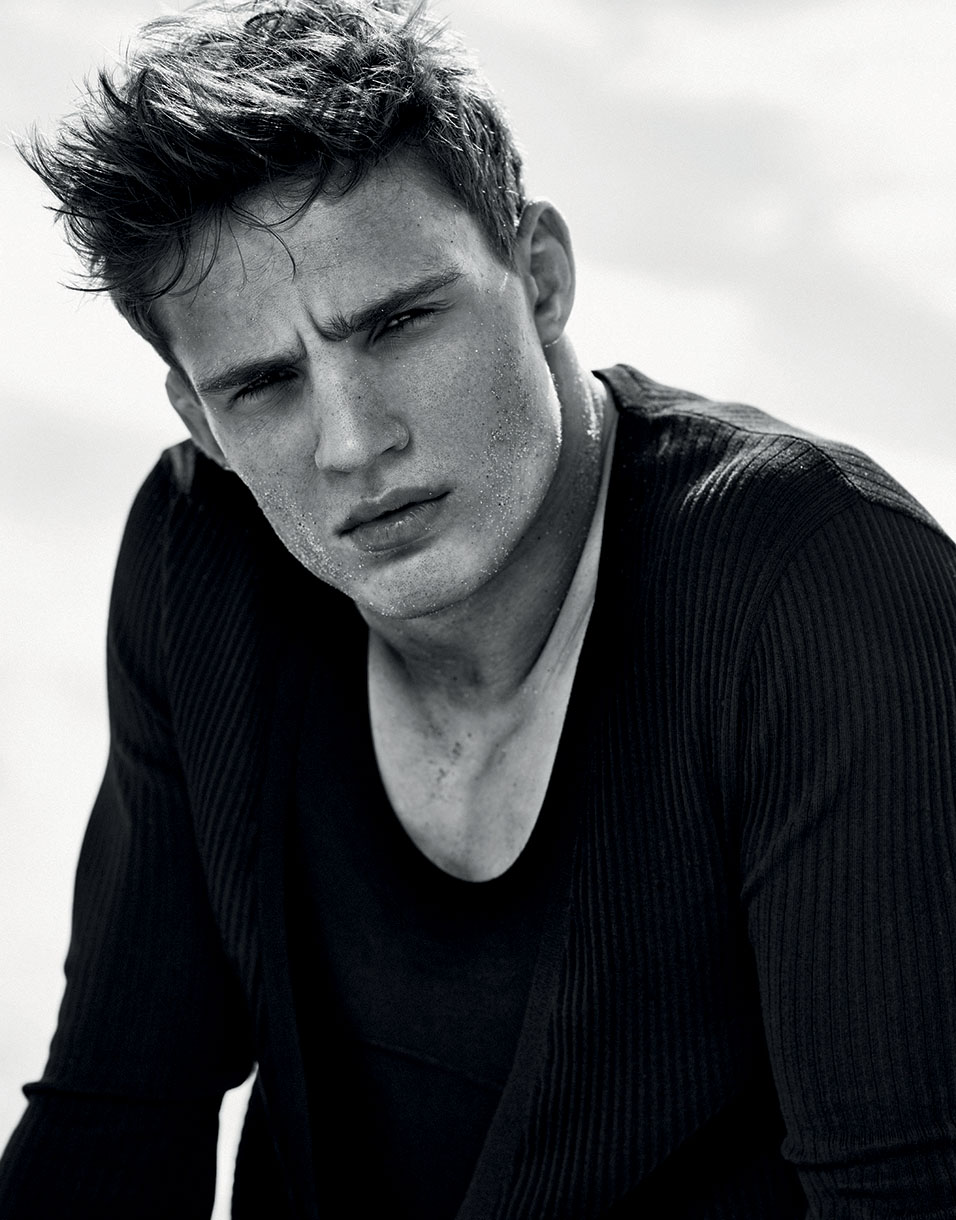 Monochromatic portrait of a handsome adult male model in a ribbed black long-sleeved shirt. His dark hair is tousled and damp.
