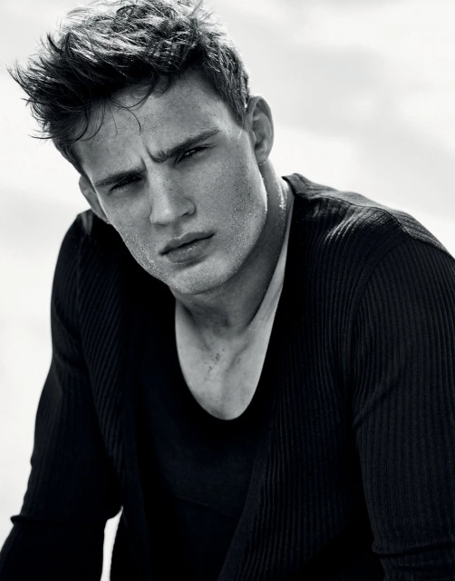 Monochromatic portrait of a handsome adult male model in a ribbed black long-sleeved shirt. His dark hair is tousled and damp. 