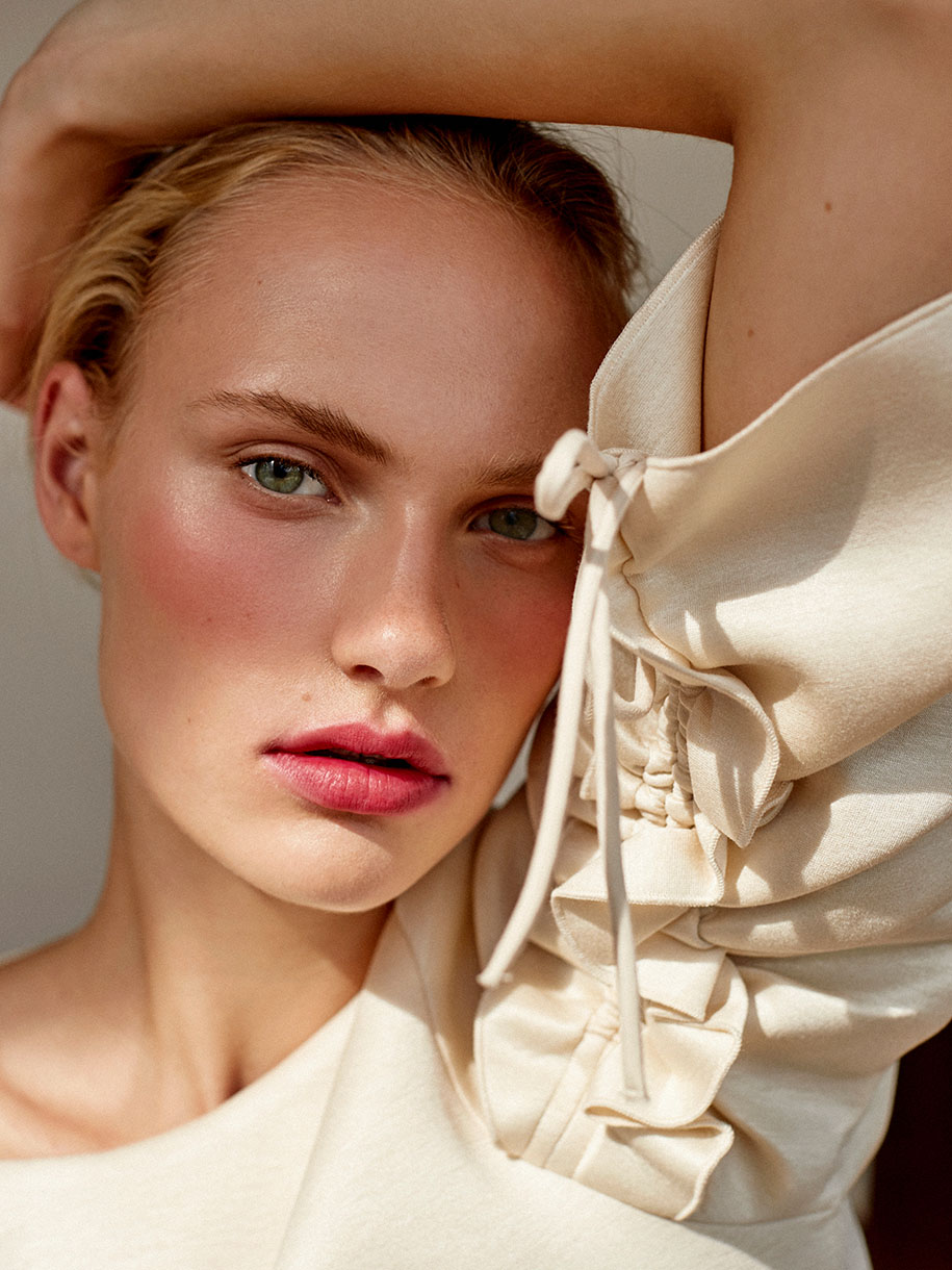 Close-up portrait of a woman with braided sleeve detail and rosy makeup with hair styled by Charlotte Niketic
