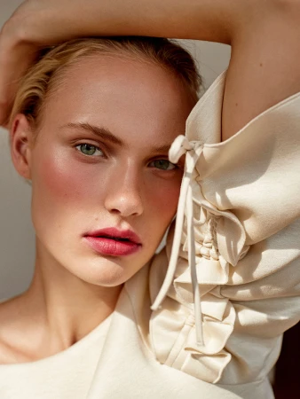 Close-up portrait of a woman with braided sleeve detail and rosy makeup with hair styled by Charlotte Niketic