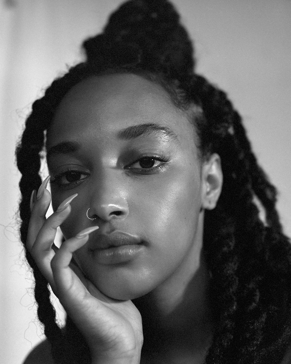 Striking black and white portrait of a woman with long dreadlocks, styled in a high bun, showcasing her face and subtle nose ring.