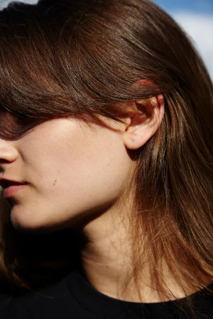 Close-up profile of a woman with long brown hair wearing a black top against a clear blue sky background.