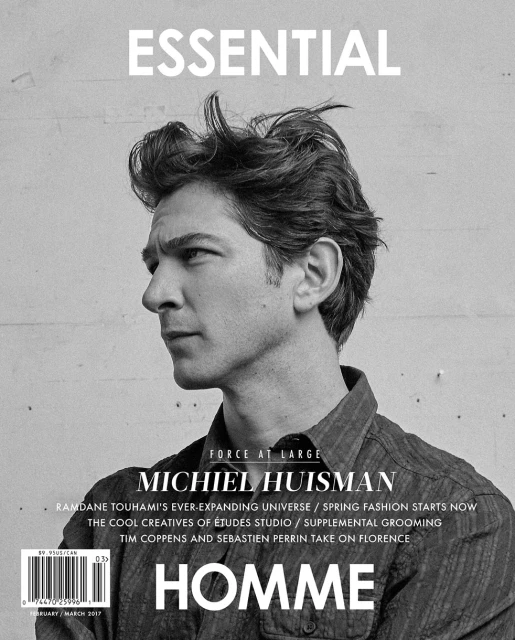 Black and white magazine cover featuring Michiel Huisman in medium shot, hair tousled, wearing a collared shirt against concrete.