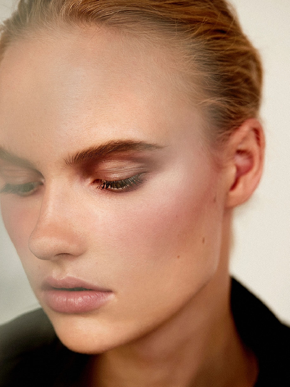 Close-up beauty shot of a fair-skinned adult woman with light brown hair and neutral makeup, wearing a black jacket indoors.