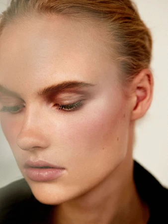 Close-up beauty shot of a fair-skinned adult woman with light brown hair and neutral makeup, wearing a black jacket indoors.
