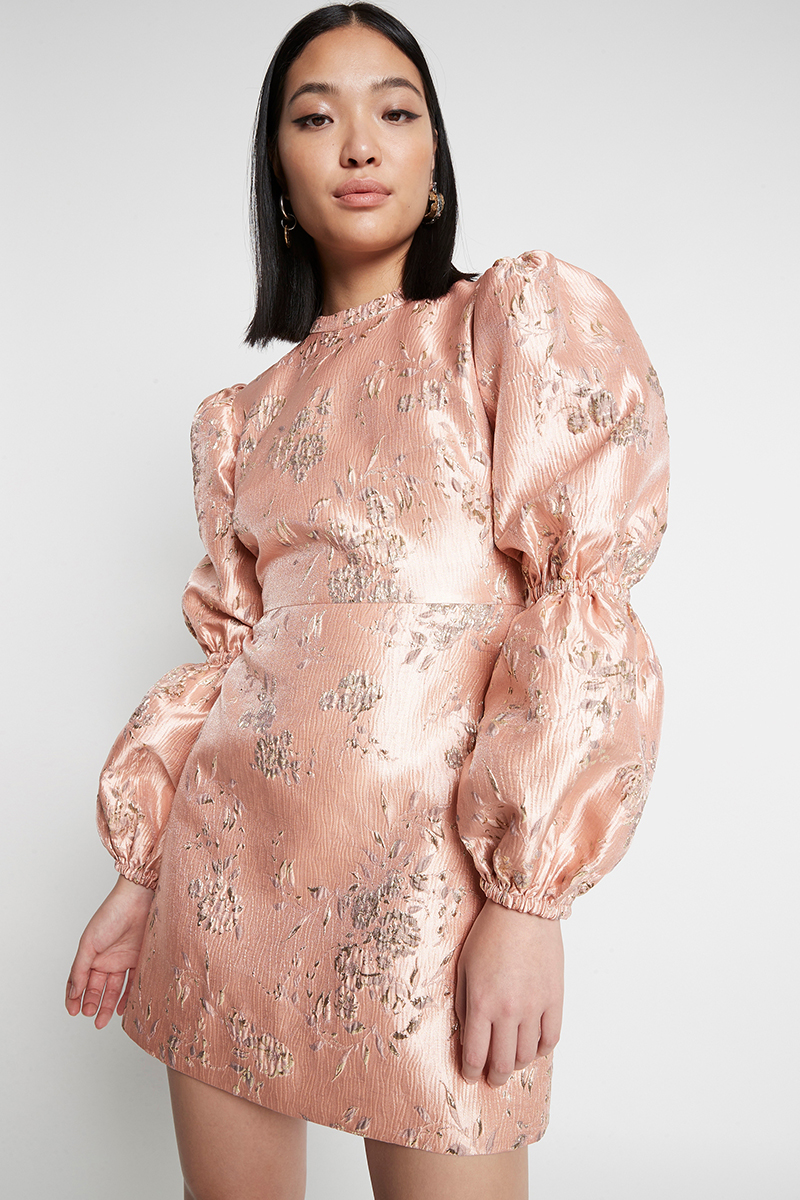 Elegant Asian woman wears a pale pink, floral-patterned mini dress with puff sleeves in a studio shot against a white backdrop.