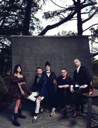 Group of five people posed in front of an outdoor grey backdrop with trees framing the scene in Sydney.