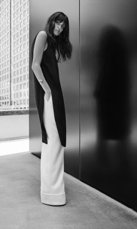 Model in black sleeveless top and white trousers posing against a dark wall in Sydney, retouched by Silvija Mandic.