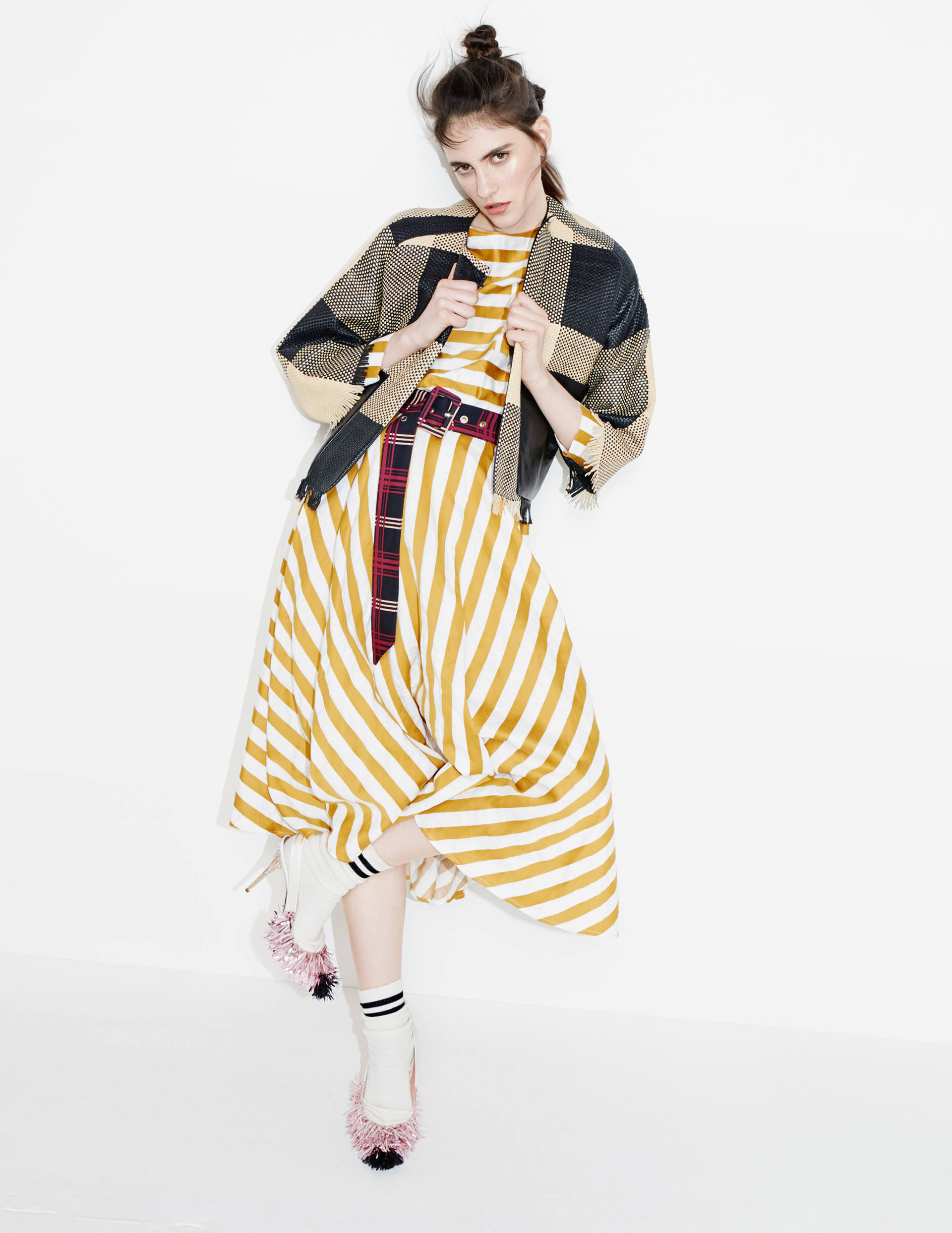 Model in yellow striped dress and plaid jacket posing against a white seamless background