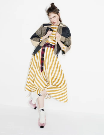 Model in yellow striped dress and plaid jacket posing against a white seamless background