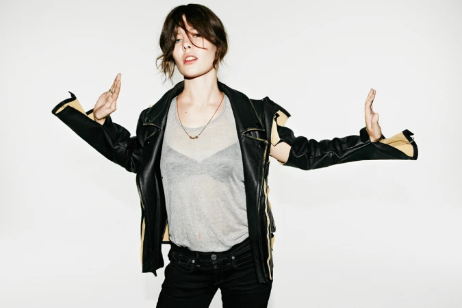Woman wearing a black leather jacket over a grey t-shirt holding her hands up against a white background