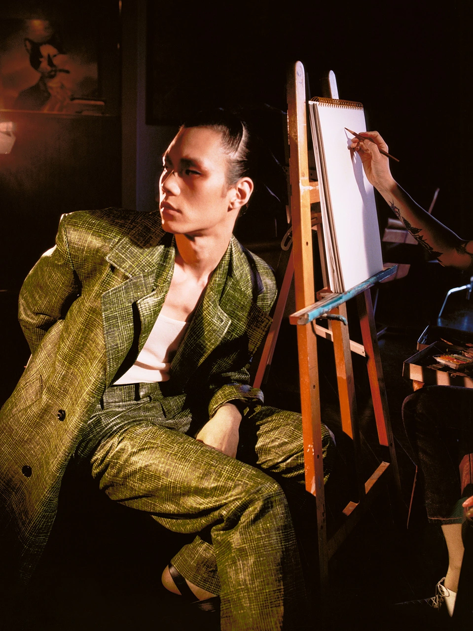 An Asian man in a green textured suit sitting near an artist easel in Sydney captured by photographer Ted Min