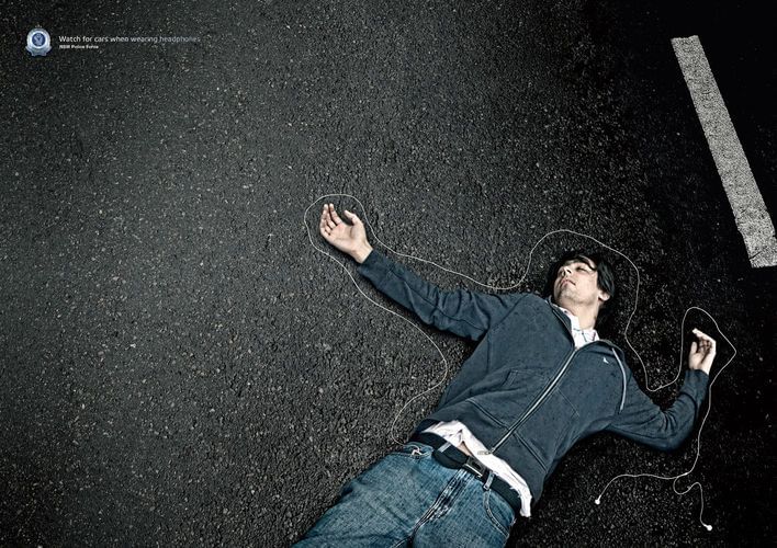 Man lies in chalk outline on pavement with headphones, conveying a dark message about pedestrian safety and distracted walking.