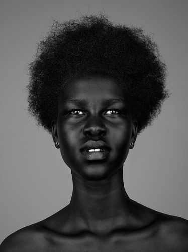 Monochrome portrait of a black woman with an afro hairstyle and neutral expression against a plain grey background