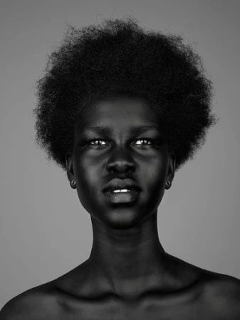 Monochrome portrait of a black woman with an afro hairstyle and neutral expression against a plain grey background