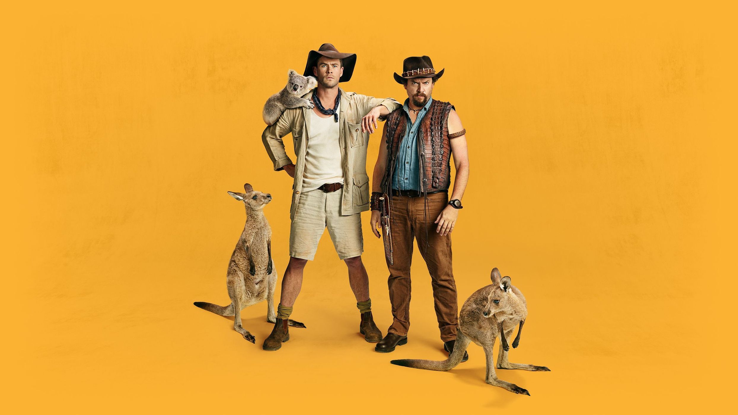 Two men in hats pose with koala and kangaroos on yellow backdrop, evoking an Australian outback or wildlife scene, medium shot.