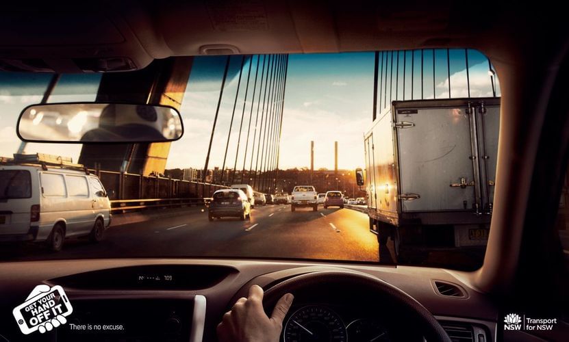 Car interior view of traffic on a bridge at sunset, emphasizing safe driving. Ad shows an interior car shot and road with other cars.